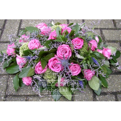 Roze ovaal rouwarrangement van vel gekleurde roze rozen en blauwe accenten